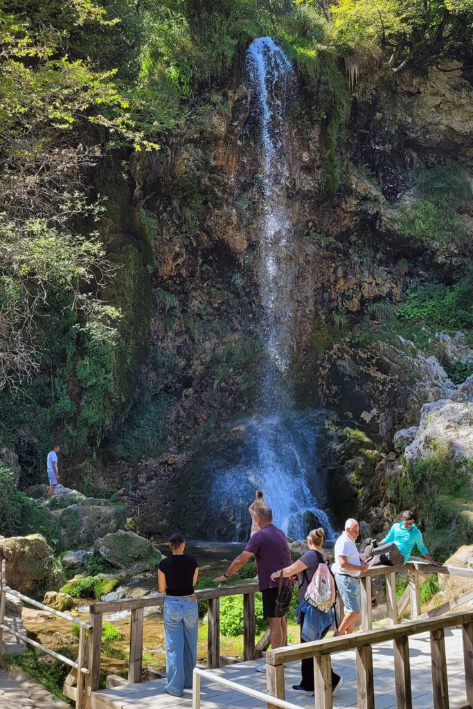 Besucher blicken von einem Aussichtspunkt auf den Gostilje-Wasserfall – City-Check Zlatibor, FemNews.de Wasser fließt über moosbedeckte Kalkfelsen am Gostilje-Wasserfall.